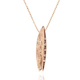 In this photo there is a rose gold surfboard pendant with diamonds and hand engravings.
