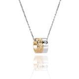 This picture shows a 14k yellow and white gold two-tone barrel pendant with hand engravings and a diamond.