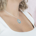 In this photo there is a model turned to the right with blonde hair and a white shirt, wearing a sterling silver compass pendant with blue larimar, blue opalite, and topaz gemstones.