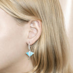 The picture shows a model wearing a 925 sterling silver larimar eagle ray lever-back earring with topaz