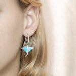 The picture shows a model wearing a 925 sterling silver larimar eagle ray lever-back earring with topaz