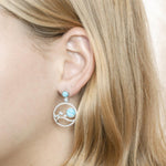 In this photo there is a model wearing 925 sterling silver earrings with blue larimar, aquamarine, and topaz gemstones.