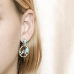 In this photo there is a model wearing 925 sterling silver earrings with blue larimar, aquamarine, and topaz gemstones.
