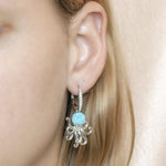 The picture shows a model wearing a 925 sterling silver larimar octopus lever-back earring with topaz and aquamarine gemstones.