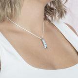 In this picture there is a model with blonde hair and a white shirt turned to the right wearing a lighthouse pendant with blue larimar gemstones set in sterling silver.