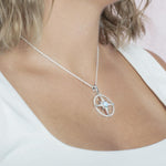 In this photo there is model turned to the right with blonde hair and a white shirt, wearing a sterling silver compass pendant with blue larimar and topaz gemstones.