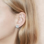 In this photo there is a model wearing a 925 sterling silver pikake flower stud earring with blue larimar gemstones.