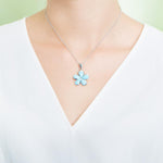 In this photo there is a model with a white shirt wearing a medium sized sterling silver plumeria pendant with blue larimar gemstones.