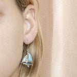 In this photo is a model wearing a 925 sterling silver sailboat hook earring with blue larimar and topaz gemstones.