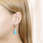 The picture shows a model wearing a 925 sterling silver larimar starry sky teardrop lever-back earring with topaz.