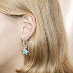 The picture shows a model wearing a 925 sterling silver larimar swimming sea turtle lever-back earring.
