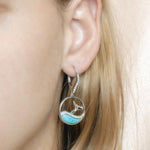 The picture shows a model wearing a 925 sterling silver larimar whale wave lever-back earring with topaz.