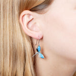 In this photo there is close-up of a model with blonde hair wearing a pair of sterling silver dragonfly dangle earrings with blue opalite gemstones.