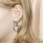 The picture shows a model wearing a 925 sterling silver pavé larimar sea turtle earring.