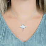 The picture shows a model wearing a 925 sterling silver, white gold vermeil, pavé manta ray pendant with topaz.