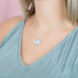 The picture shows a model wearing a 925 sterling silver, white gold vermeil, pavé manta ray pendant with topaz.