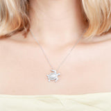 The picture shows a model wearing a 925 sterling silver, white gold plated, sea turtle pendant with topaz.