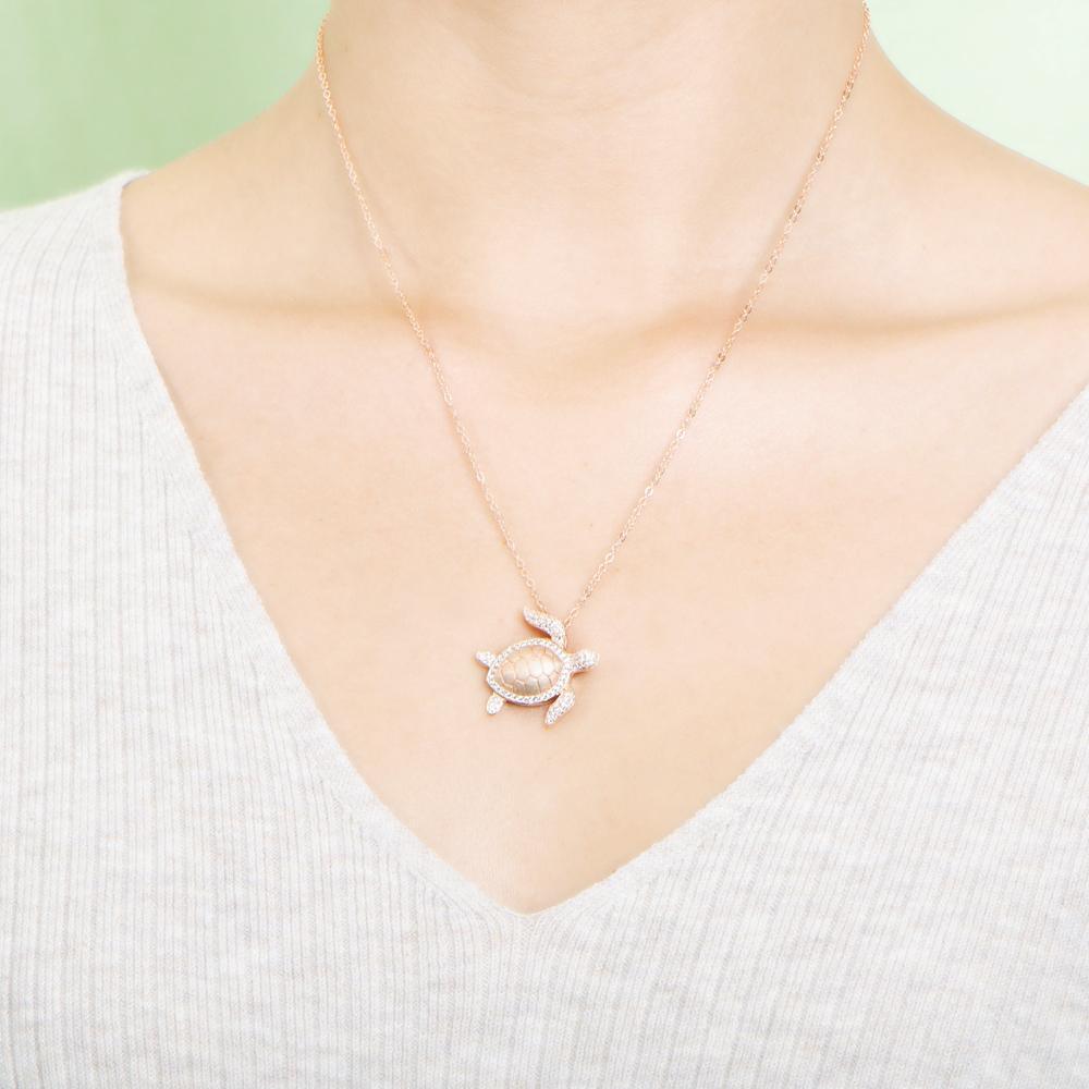 The picture shows a model wearing a 925 sterling silver, rose gold plated, sea turtle pendant with topaz.