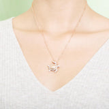 The picture shows a model wearing a 925 sterling silver, rose gold plated, sea turtle pendant with topaz.