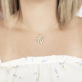 In this photo there is a model with blonde hair and a white shirt with flowers, wearing a yellow gold palm tree pendant with topaz gemstones.
