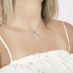 In this photo there is a model turned slightly to the right with blonde hair and a white shirt with flowers, wearing a white gold palm tree pendant with topaz gemstones.