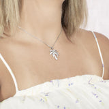 In this photo there is a model turned slightly to the right with blonde hair and a white shirt with flowers, wearing a white gold palm tree pendant with topaz gemstones.