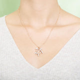 In this photo there is a model with blonde hair and a white shirt, wearing a rose gold sea turtle pendant with topaz gemstones.