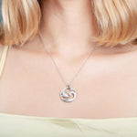 The picture shows a model wearing a 925 sterling silver, white gold vermeil, dolphin and wave pendant with topaz.