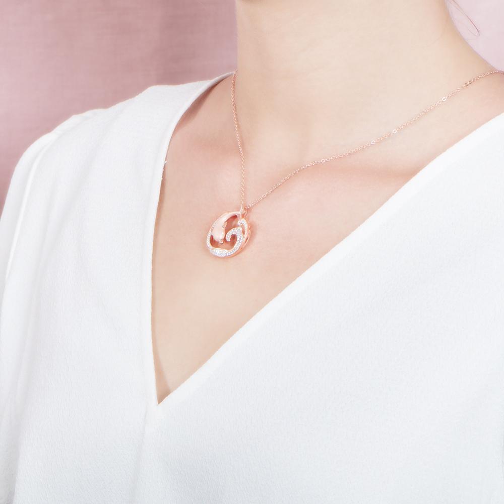 The picture shows a model wearing a 925 sterling silver, rose gold vermeil, dolphin and wave pendant with topaz.