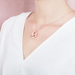 The picture shows a model wearing a 925 sterling silver, rose gold vermeil, dolphin and wave pendant with topaz.