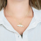 The picture shows a model wearing a 925 sterling silver, yellow gold vermeil, pavé whale tail pendant with topaz.
