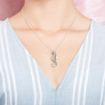 In this photo there is a model with a light blue and white striped shirt, wearing a sterling silver seahorse pendant.