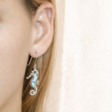 The picture shows a model wearing a 925 sterling silver larimar seahorse hook earring with topaz.