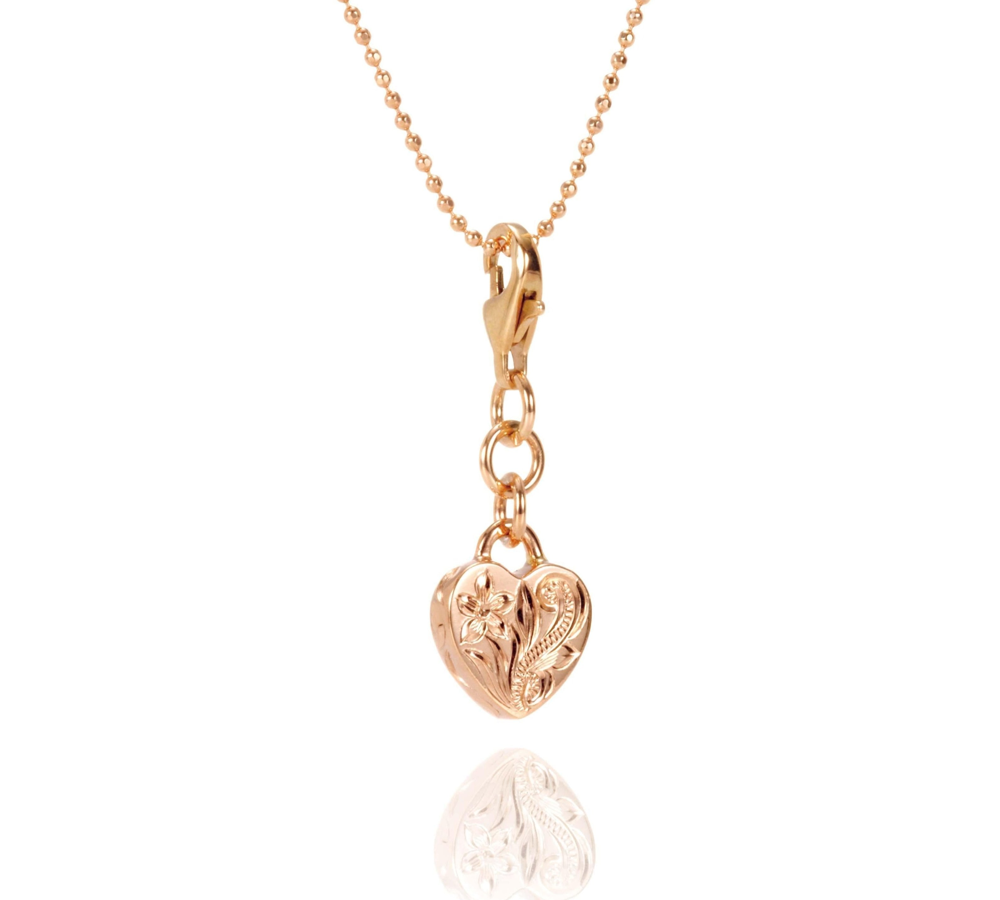 In this photo there is a 14k rose gold heart charm with plumeria engraving.