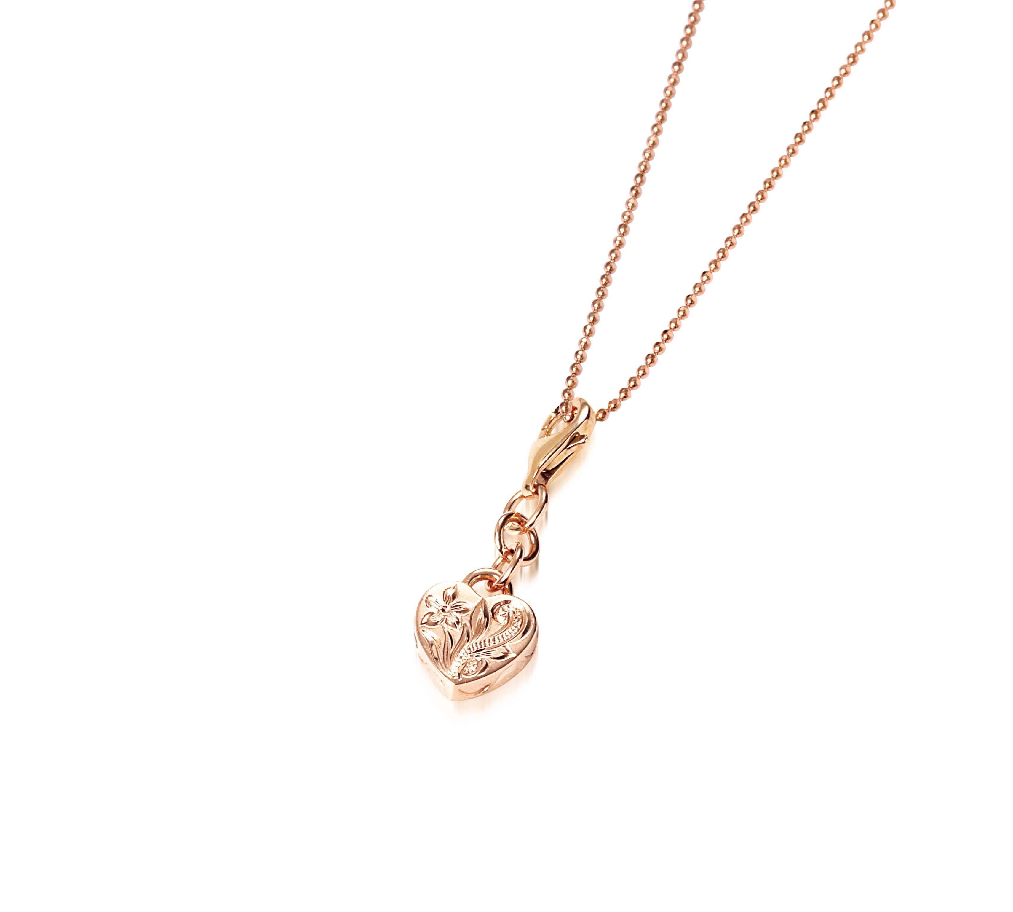In this photo there is a 14k rose gold heart charm with plumeria engraving.