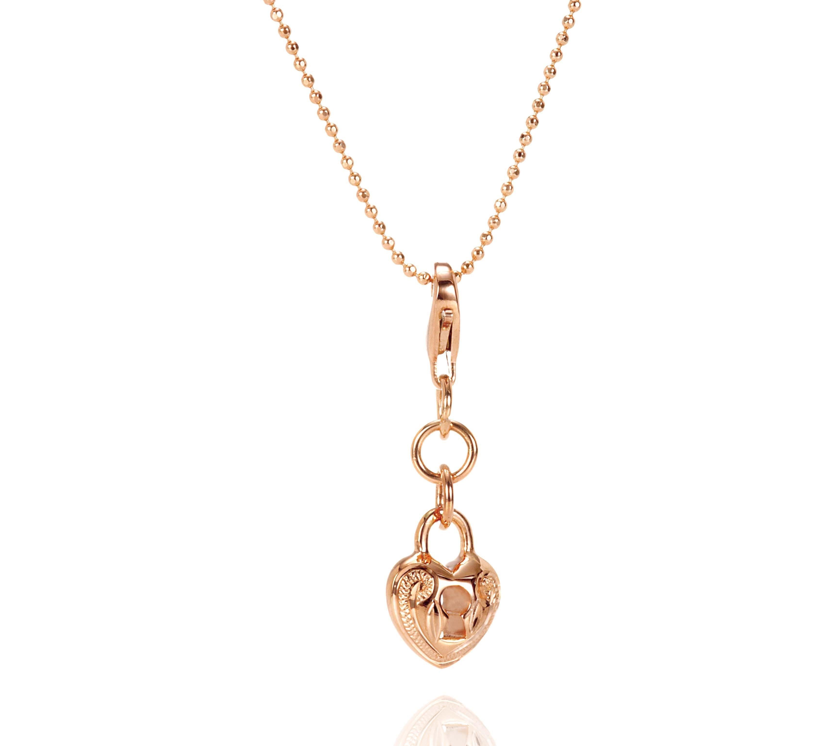 The picture shows a 14K rose gold heart lock charm with hand-engraved detailing.