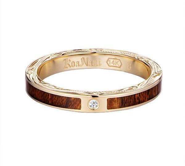 In this photo there is a yellow gold koa wood ring with hand engravings of scrolls and one diamond.
