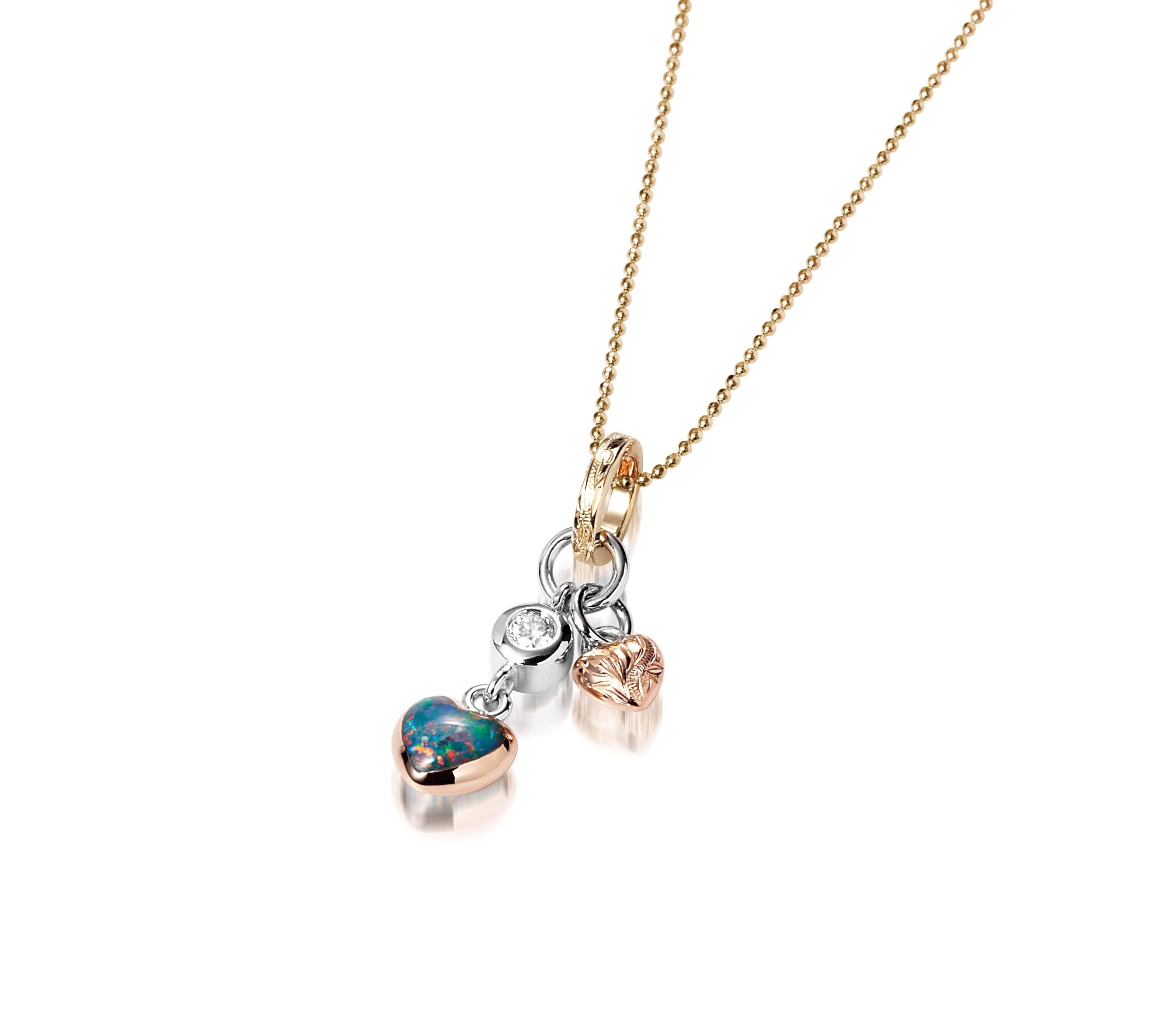 The picture shows a 14K yellow, white, and rose gold opal two-heart charm pendant with hand engravings and a diamond.