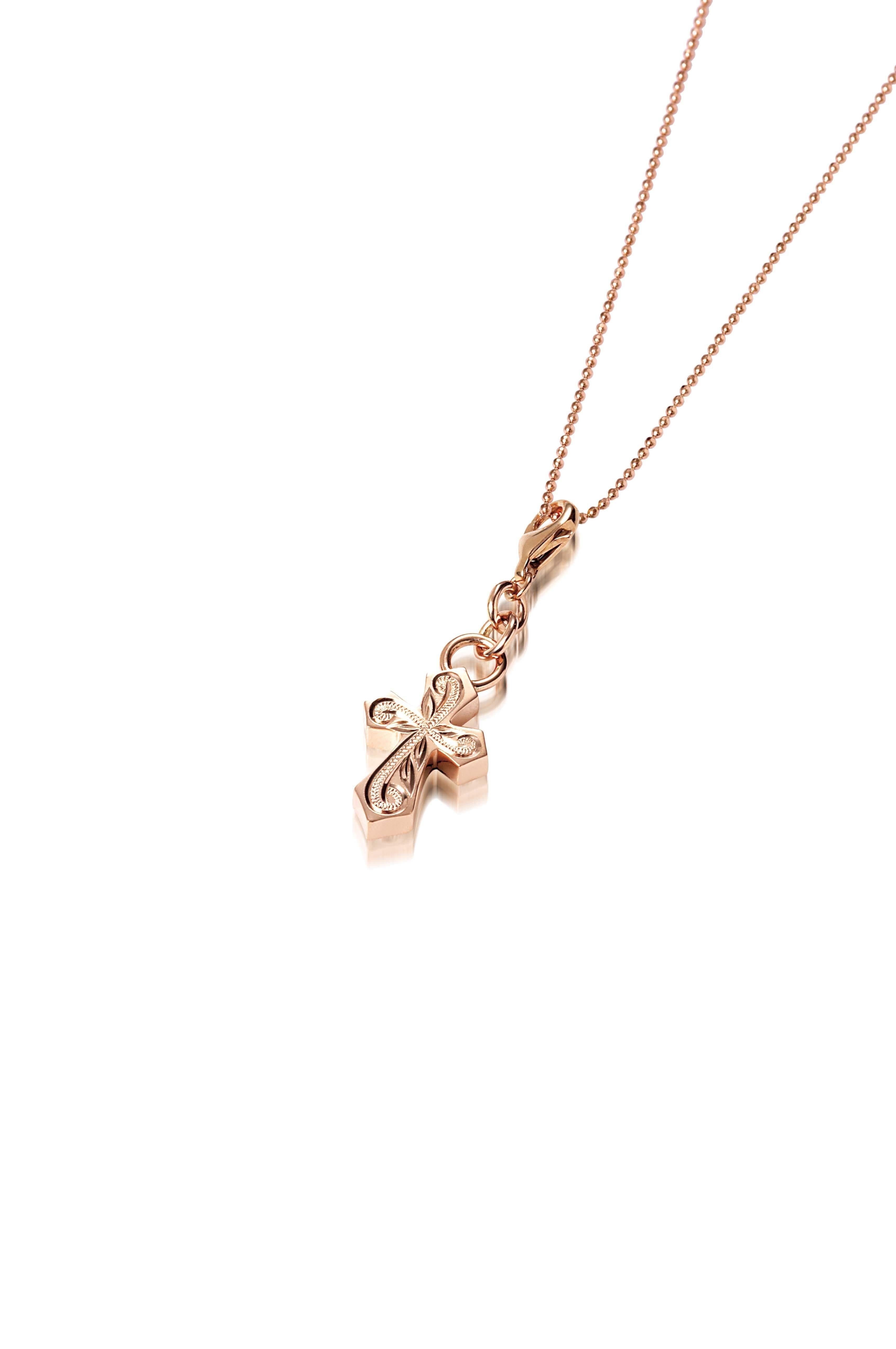 The picture shows a 14K rose gold pointed cross charm with hand-engraved detailing.