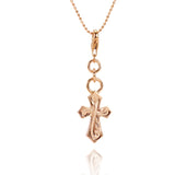 The picture shows a 14K rose gold pointed cross charm with hand-engraved detailing.