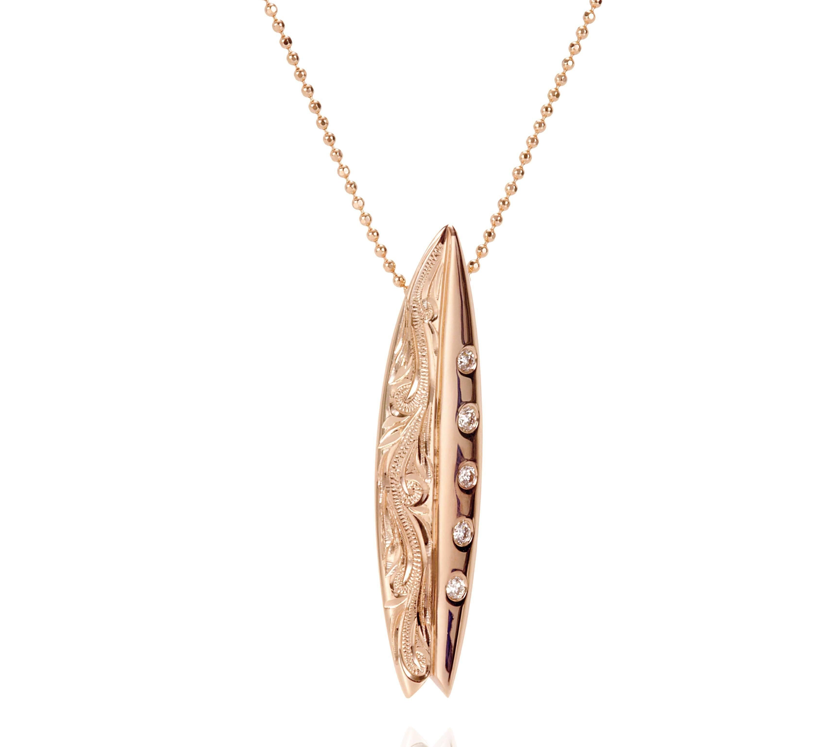 In this photo there is a rose gold surfboard pendant with diamonds and hand engravings.