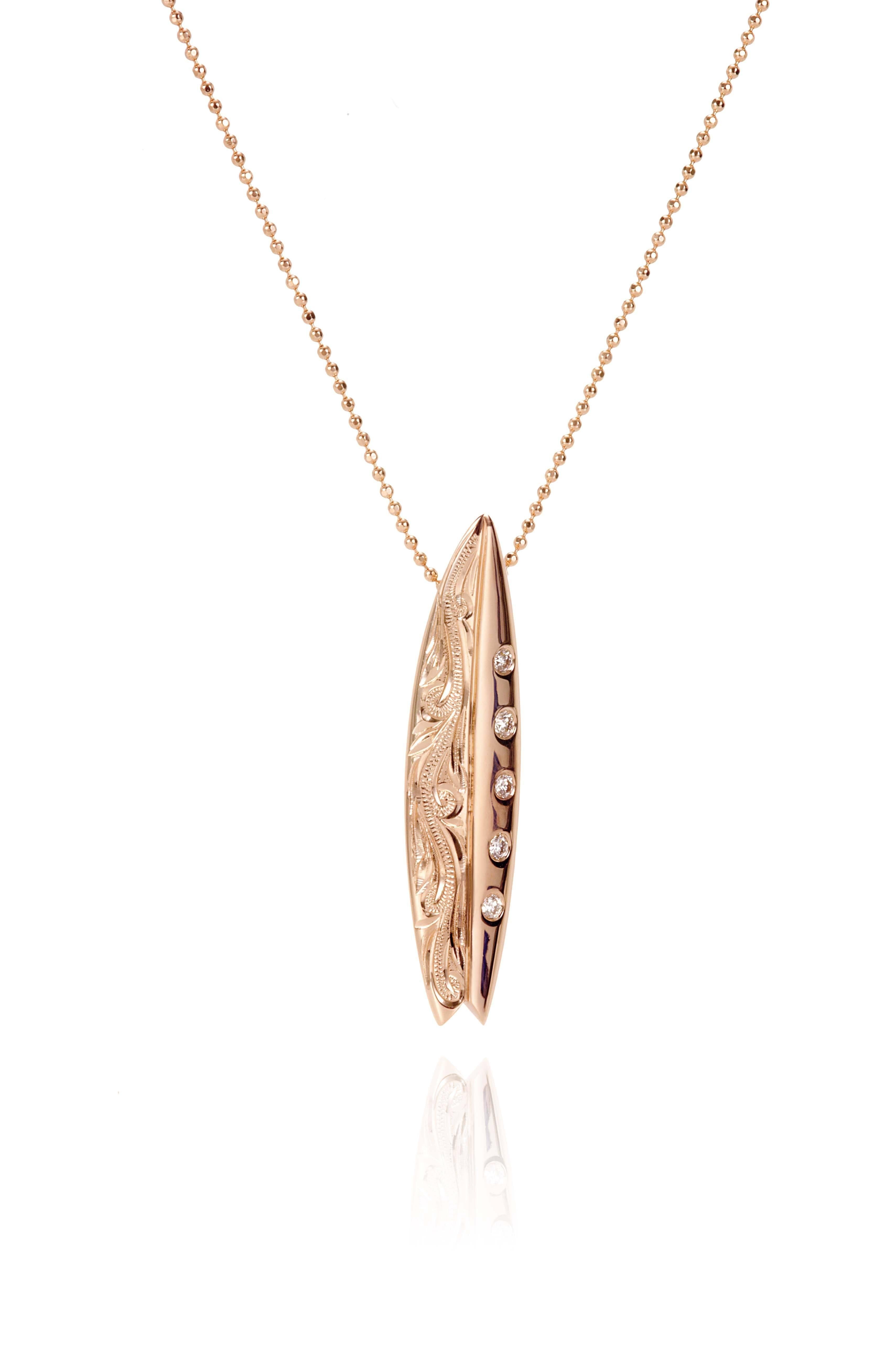 In this photo there is a rose gold surfboard pendant with diamonds and hand engravings.