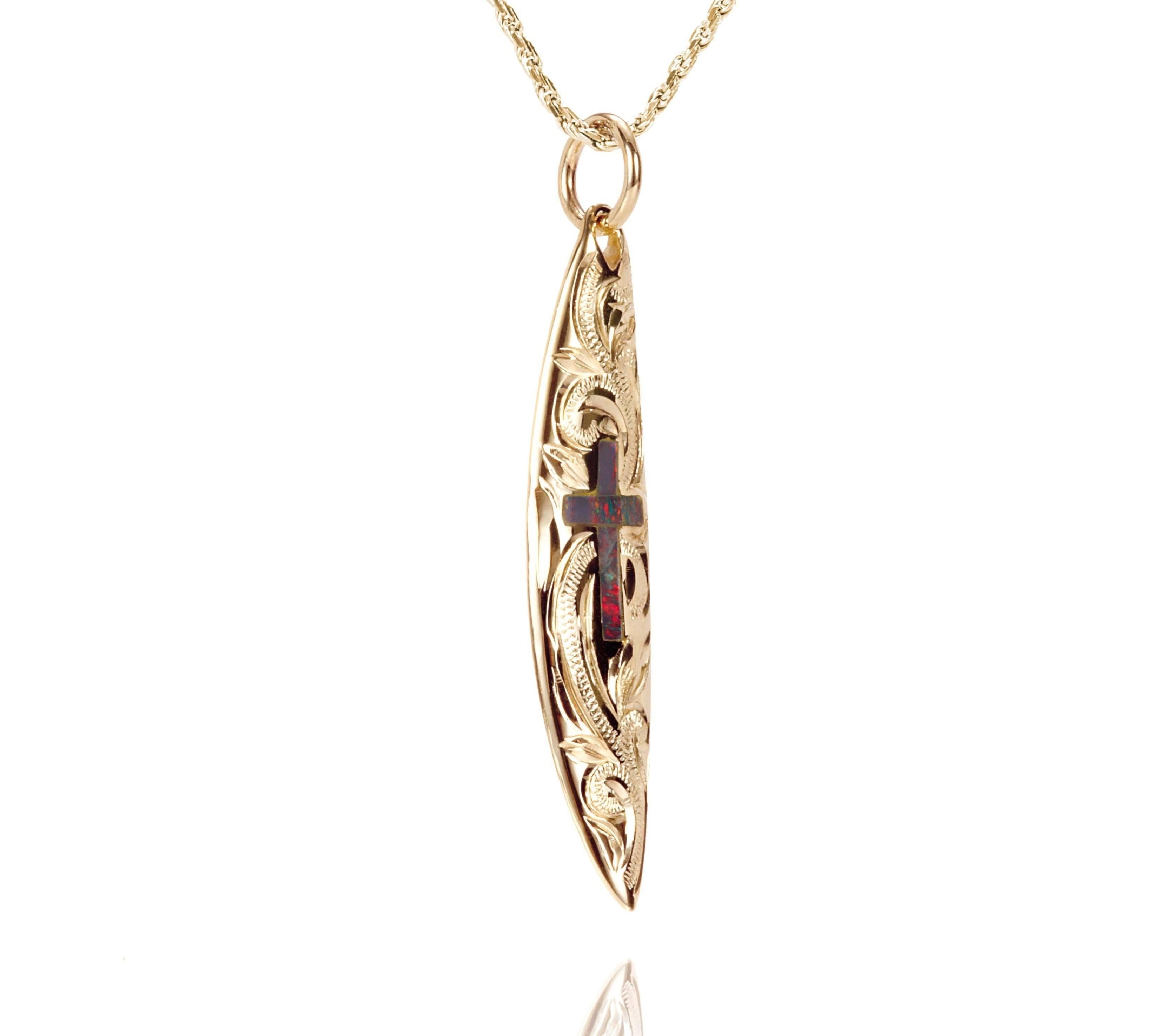 In this photo there is a yellow gold surfboard pendant with an opal cross and hand engravings.