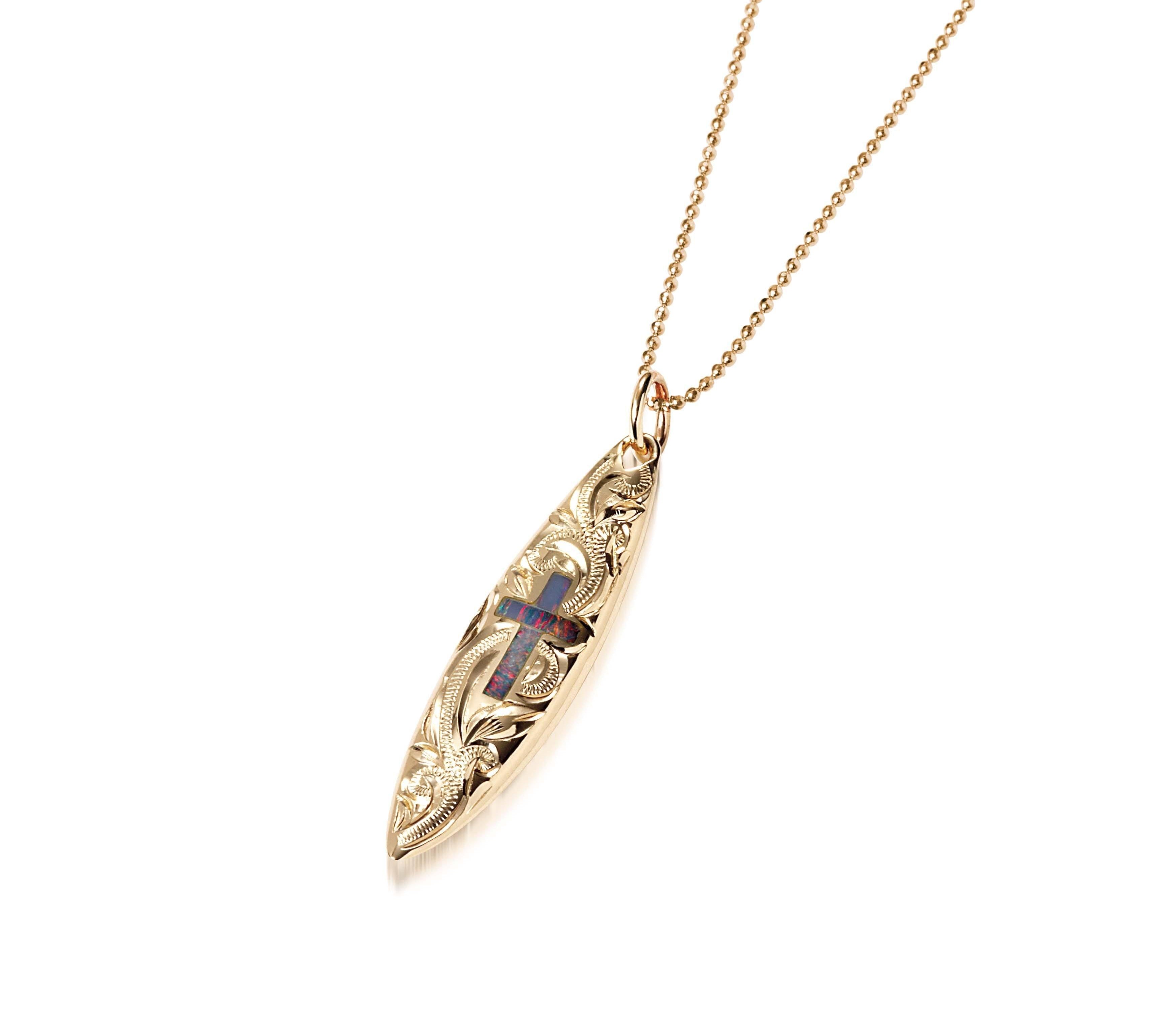 In this photo there is a yellow gold surfboard pendant with an opal cross and hand engravings.