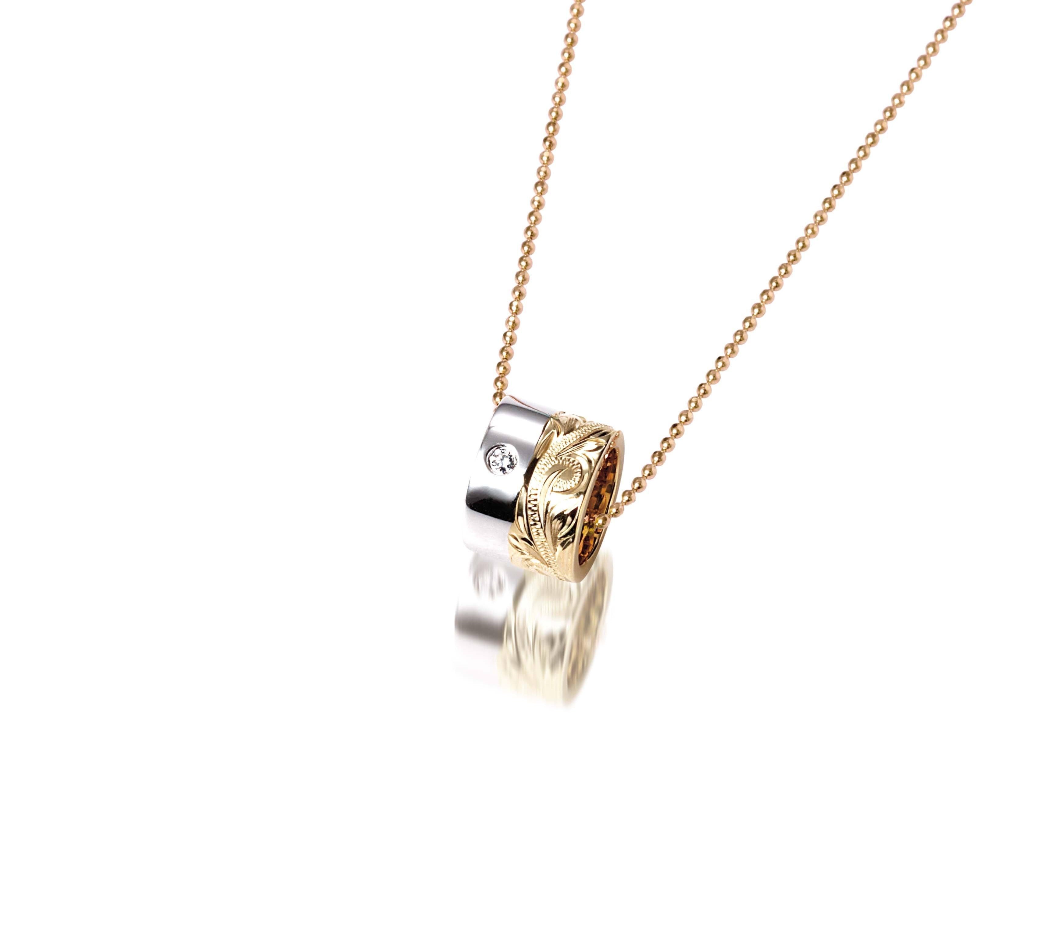 This picture shows a 14k yellow and white gold two-tone barrel pendant with hand engravings and a diamond.