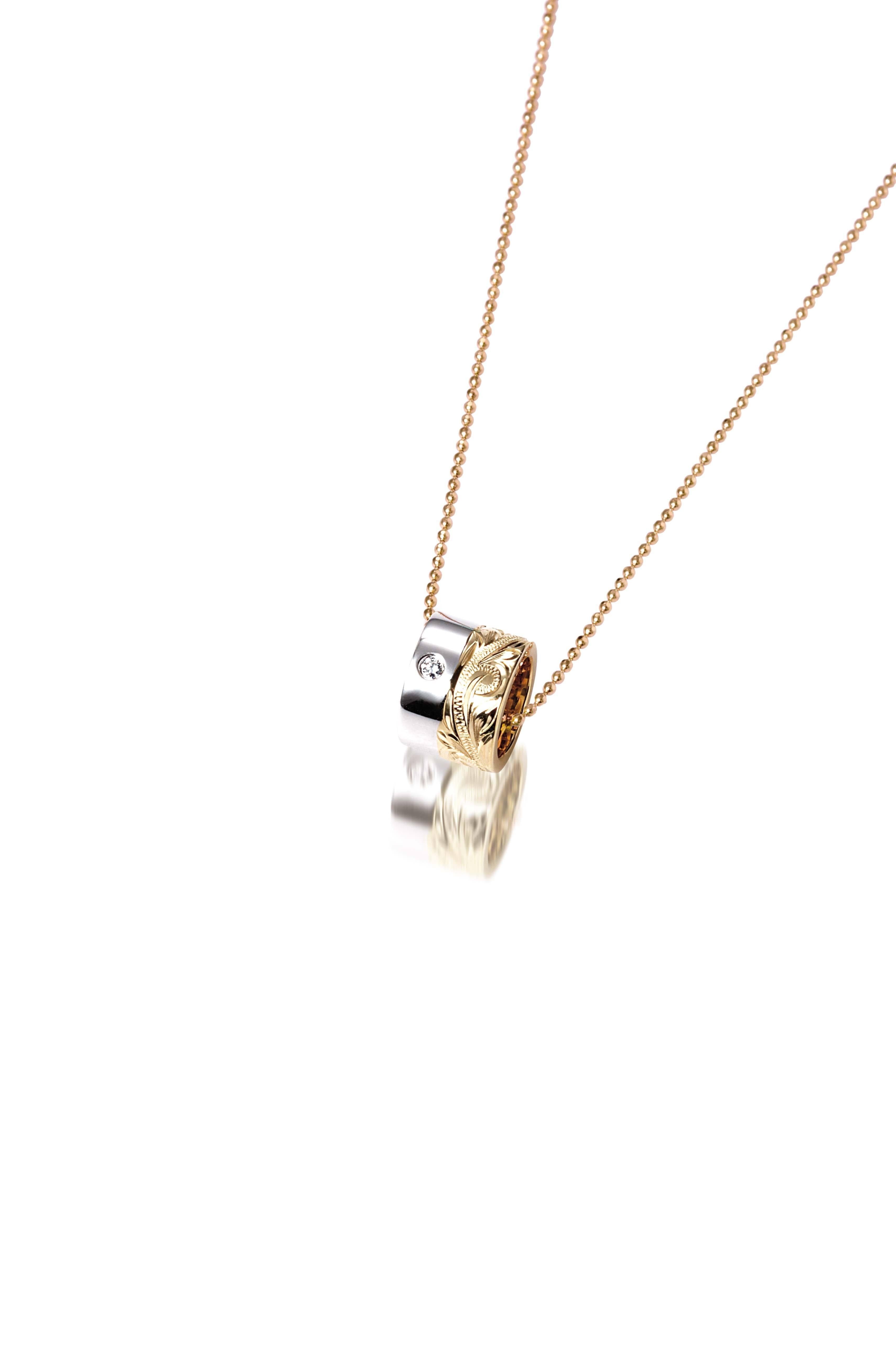 This picture shows a 14k yellow and white gold two-tone barrel pendant with hand engravings and a diamond.