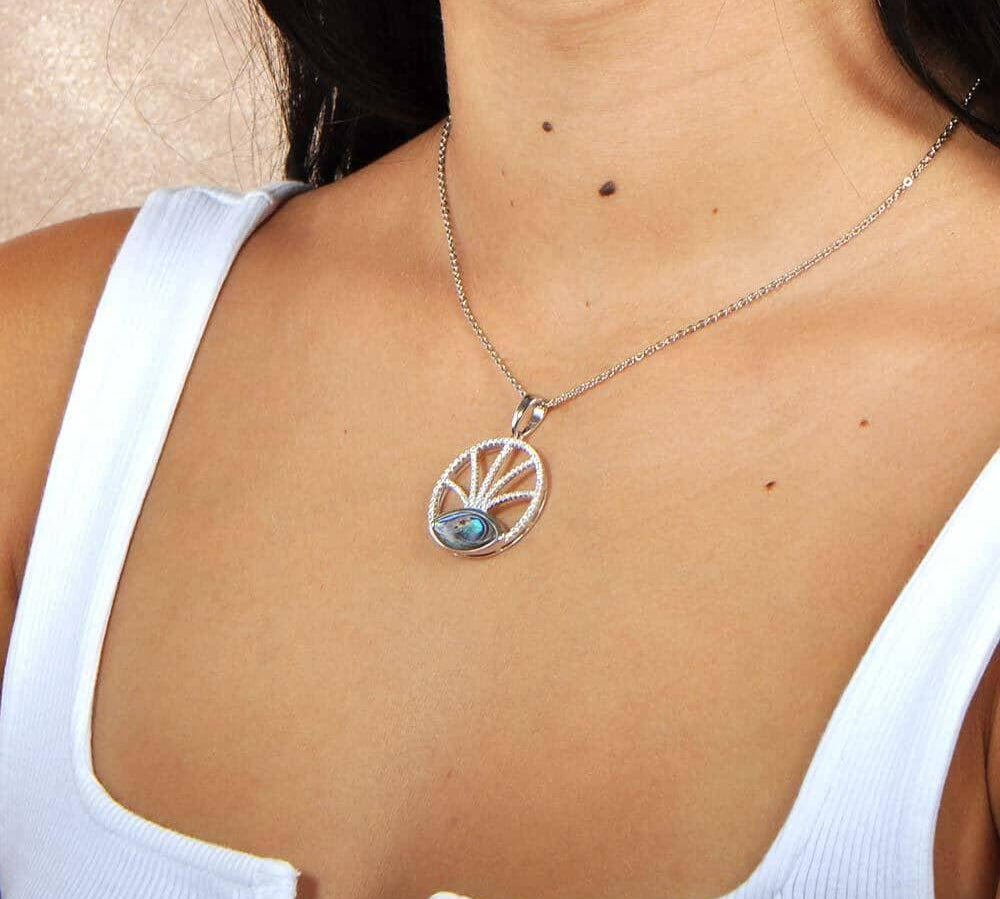 Sterling silver, white topaz, and abalone featured in a pendant with a unique design, the pendant is worn by a model. 