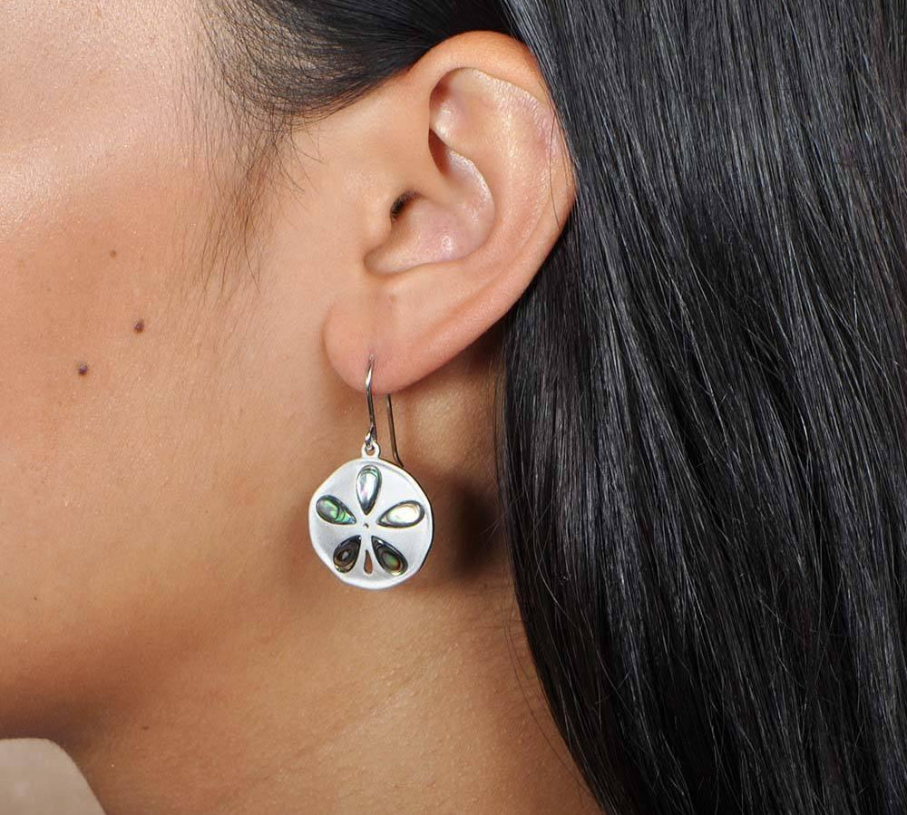 Sterling silver abalone earrings with a sand dollar design worn by a model. 