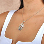 Sterling Silver, white topaz, and abole pendant designed like two dolphins. The pendant is worn by a model. 