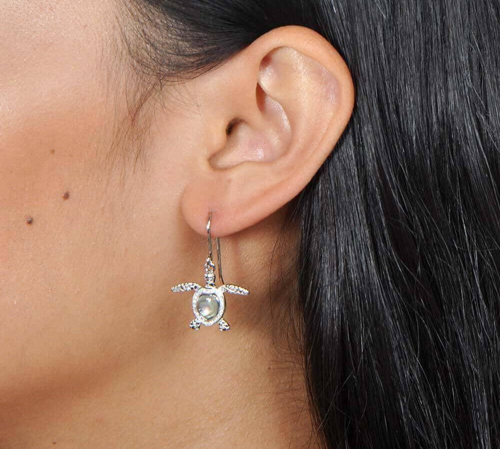 Sterling silver sea turtle hook earrings featuring Pave detail and an abalone shell. Worn by a model.